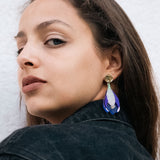 Woman with long brown hair wears a black denim jacket and handcrafted Crocus Flower Earrings, looking over her shoulder against a plain, light-colored background.